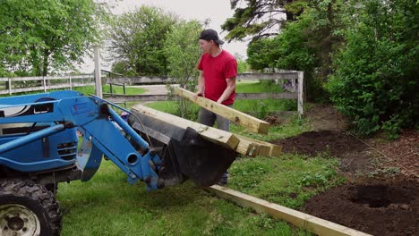 man taking out wooden poles for fence out of tractor, static view