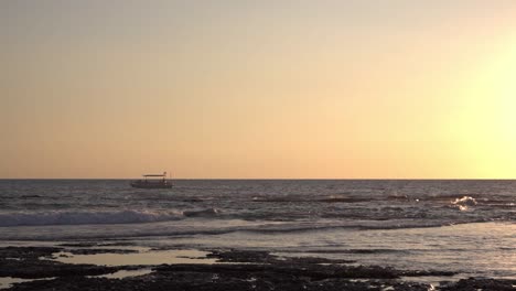 Boat-sailing-on-wavy-sea-under-picturesque-sunset-sky