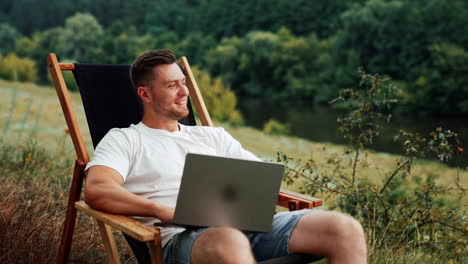 thoughtful caucasian man sits holding a laptop smiling dreamily. freelancer working remote in a comfortable natural surroundings.