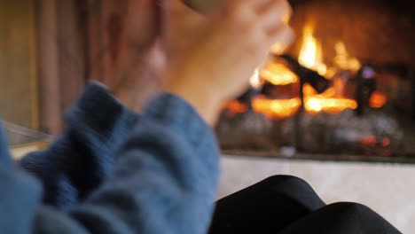 Hands-With-A-Cup-Of-Tea-In-Front-Of-A-Burning-Fireplace