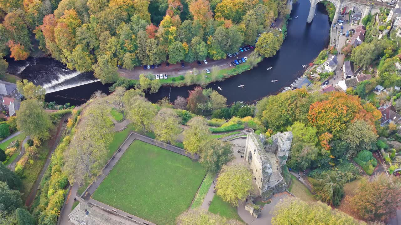 Top down view from drone shows the city Castle stone ruins, formal lawns, mature park trees, the River Nidd weir and wooded banks in the centre of Knaresborough, North Yorkshire, England