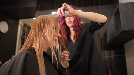 hairdresser girl with curly red hair cuts the hair of a blonde client. hairdresser girl with curly red hair cuts the hair of a blonde client. professional haircut of long hair in a beauty salon. shortening of hair. healthy looking hair