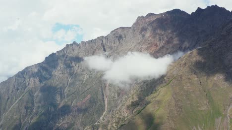 aerial drone view approaching massive mountain range and a cloud in the center of the shot