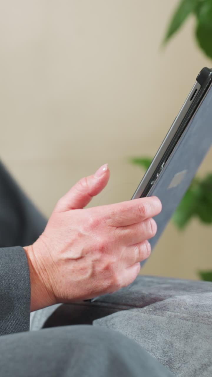 Businesswoman holding tablet with both hands while working remotely in indoor setting with green plant background, demonstrating focus, professionalism, and digital engagement in calm relaxed posture