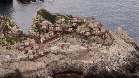 aerial drone shot showcasing beach chairs and umbrellas set on the rocks of the cliff in taormina, offering stunning views of the mediterranean sea, sicily, italy (taormina, sicilia, italia)