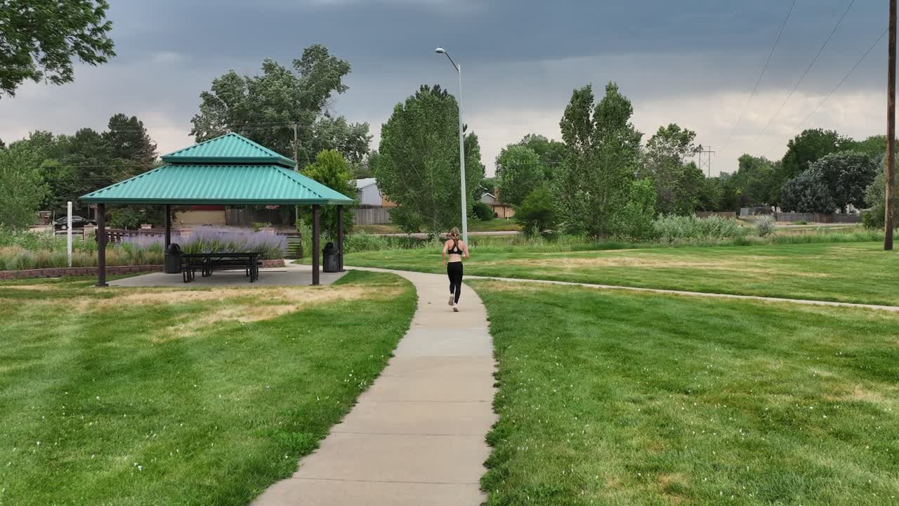 An athletic woman runs down a park pathway during stormy skies. Lean and quick she runs on a windy day with the threat of a storm in the background