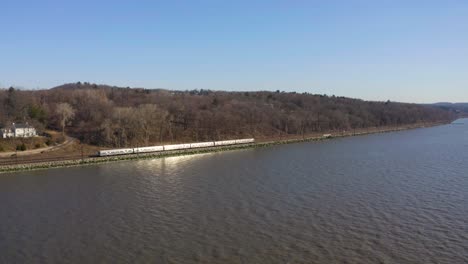 Train-passing-by-river-side-on-sunny-beautiful-day,-forest-in-background