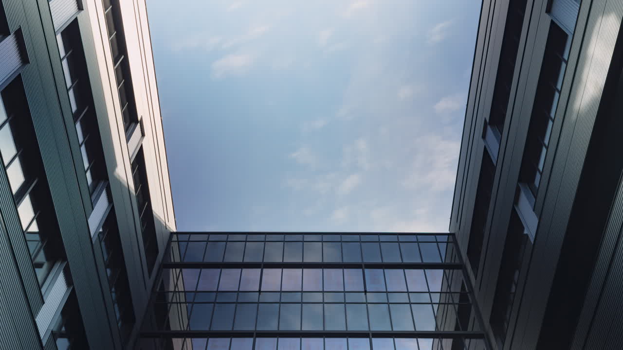 Timelapse of a modern architectural skyward view, framed by sleek office buildings with reflective glass surfaces, showcasing a bright blue sky and dynamic cloud movement on a sunny day