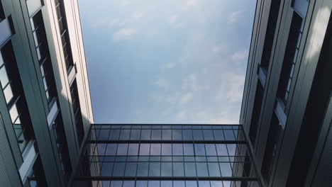 timelapse of a modern architectural skyward view, framed by sleek office buildings with reflective glass surfaces, showcasing a bright blue sky and dynamic cloud movement on a sunny day