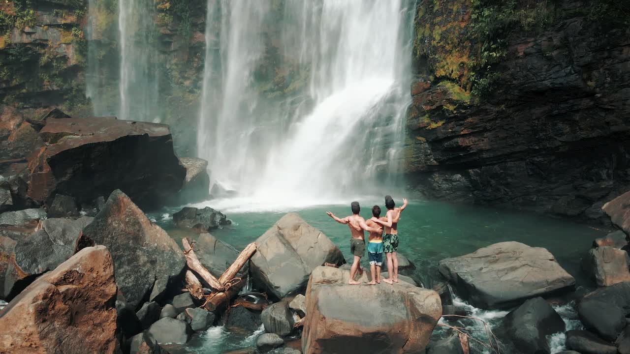 tres hombres sobre rocas con los brazos abiertos frente a la cascada nauyaca, costa rica