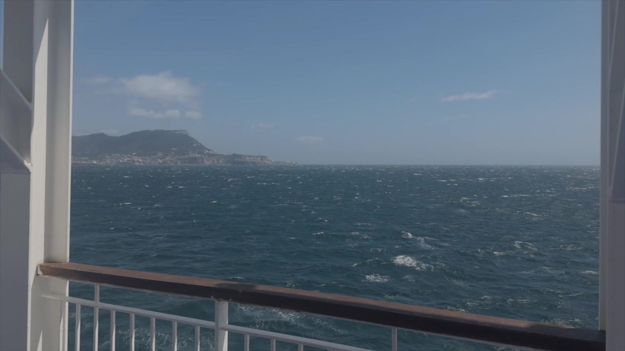 Blick vom Fährdeck mit Meereswellen und ferner Küstenlinie unter dem Himmel