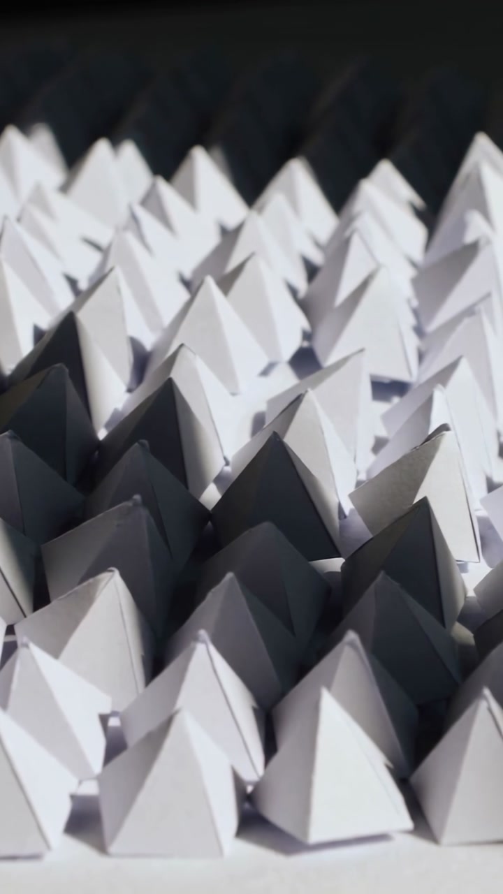 Vertical video: Frames shifting camera panning revealing paper pyramids, showing depth via shadows