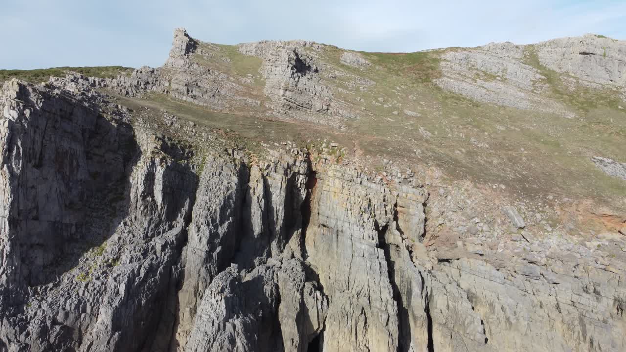 dron aéreo de ascenso lento disparado con acantilados costeros con capas de roca visibles con el camino costero de la ladera de la montaña en la península de gower reino unido 4k