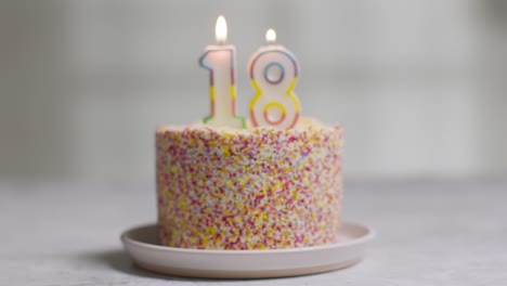 studio shot birthday cake covered with decorations and candle celebrating eighteenth birthday being blown out