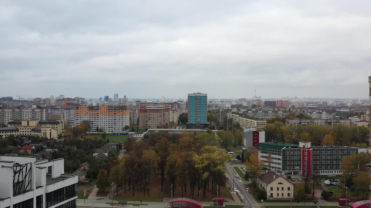 Aerial view of a modern city landscape with residential buildings, an autumn park, and street traffic under an overcast sky