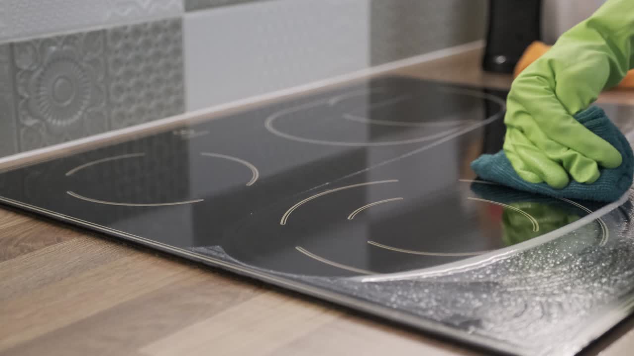 Closeup of hand woman cleaning modern cooking glass ceramic electric panel with rag
