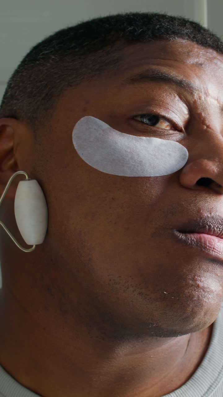 Man receiving facial treatment with jade roller and eye patches