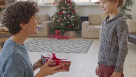 Brünette-Kurze-Haare-Mutter-Gibt-Ihrem-Sohn-Ein-Weihnachtsgeschenk-Und-Beide-Lachen-Vor-Freude