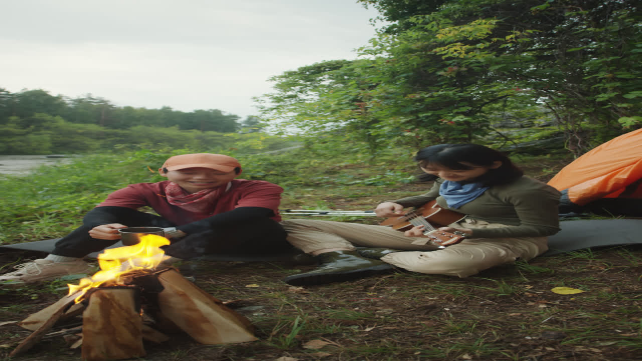 Lesbian Couple Playing Guitar by Campfire