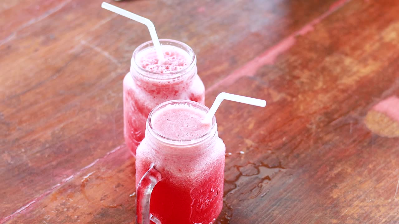Four glasses of watermelon juice are clinked together on a wooden table, creating a vibrant and refreshing scene