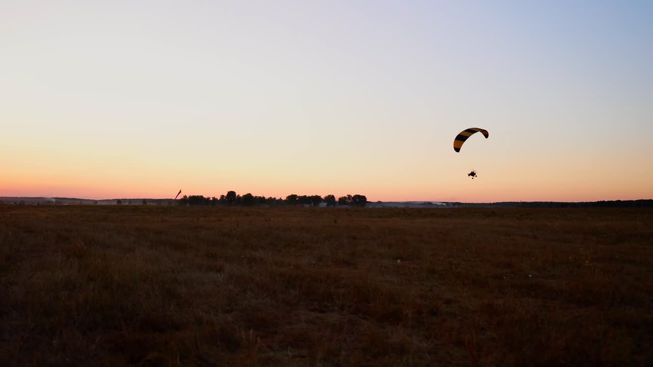 piloto volando un parapente con un motor al atardecer, la cámara en la suspensión se mueve a lo largo del campo