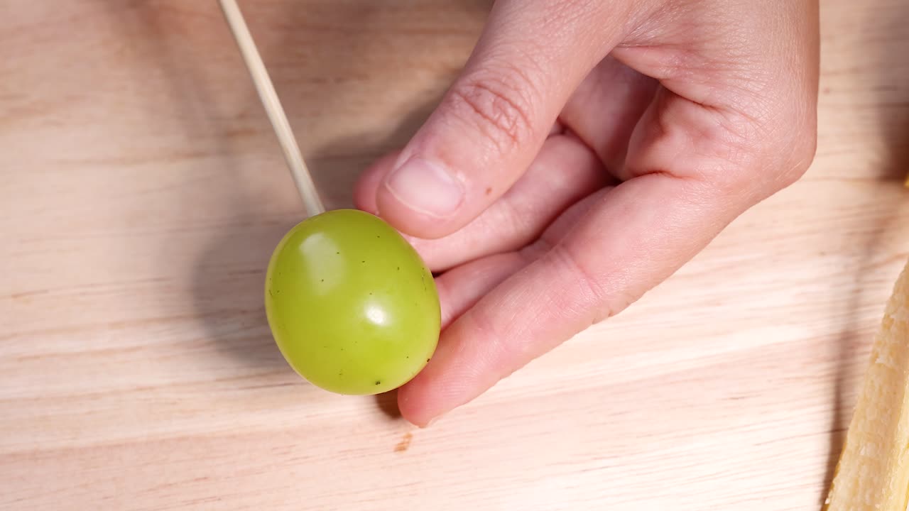 Hand skewers grape on wooden surface