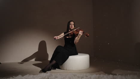 violinist in a black dress playing violin under snow