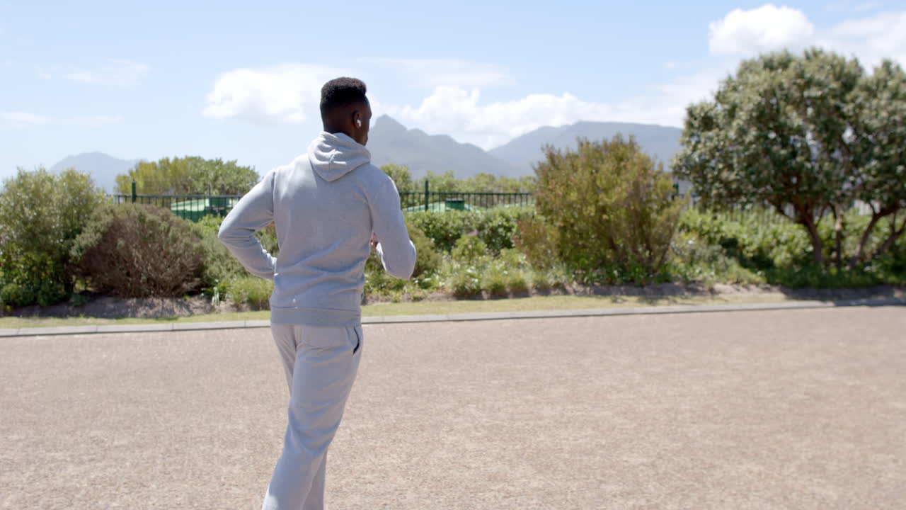 Focused african american man jogging with headphones on street on sunny day, slow motion