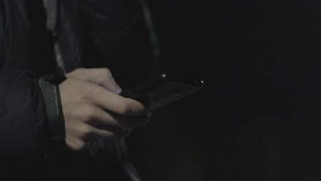 Man-scrolls-phone-in-street-at-night