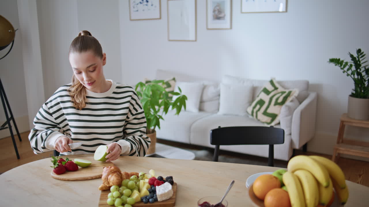 Calm woman slicing apple in bright modern kitchen. Relaxed lady preparing food