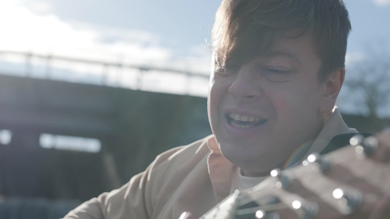 바위의 배경에 산의 강변에 앉아 기타를 연주하는 젊은이. 자유의 개념, 휴식 장소.