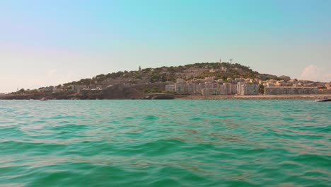 view from boat cruising along the coast of sète in southern france, with hillside houses and turquoise mediterranean waters under a clear sky