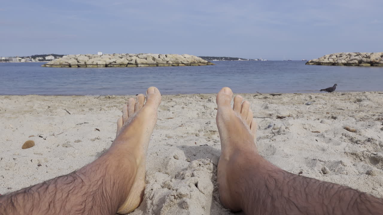 Close up of a man's wet and sandy feet on a beach with a view of the sea