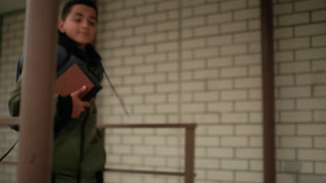 boy runs to class holding notebook under arm full of energy smiling with confidence backpack on shoulder passing tall official buildings in background showing determination and school life spirit