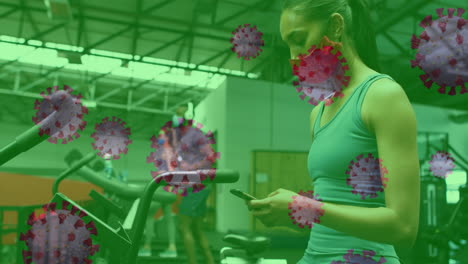 células de covid-19 flotando contra una mujer que usa una máscara facial usando un teléfono inteligente en el gimnasio