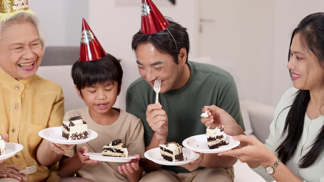 Multigenerational Asian family celebrating a birthday with cake, party hats, and laughter in living room