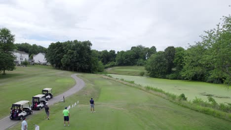 golfer hits tee shot over swampy pond, aerial drone rise