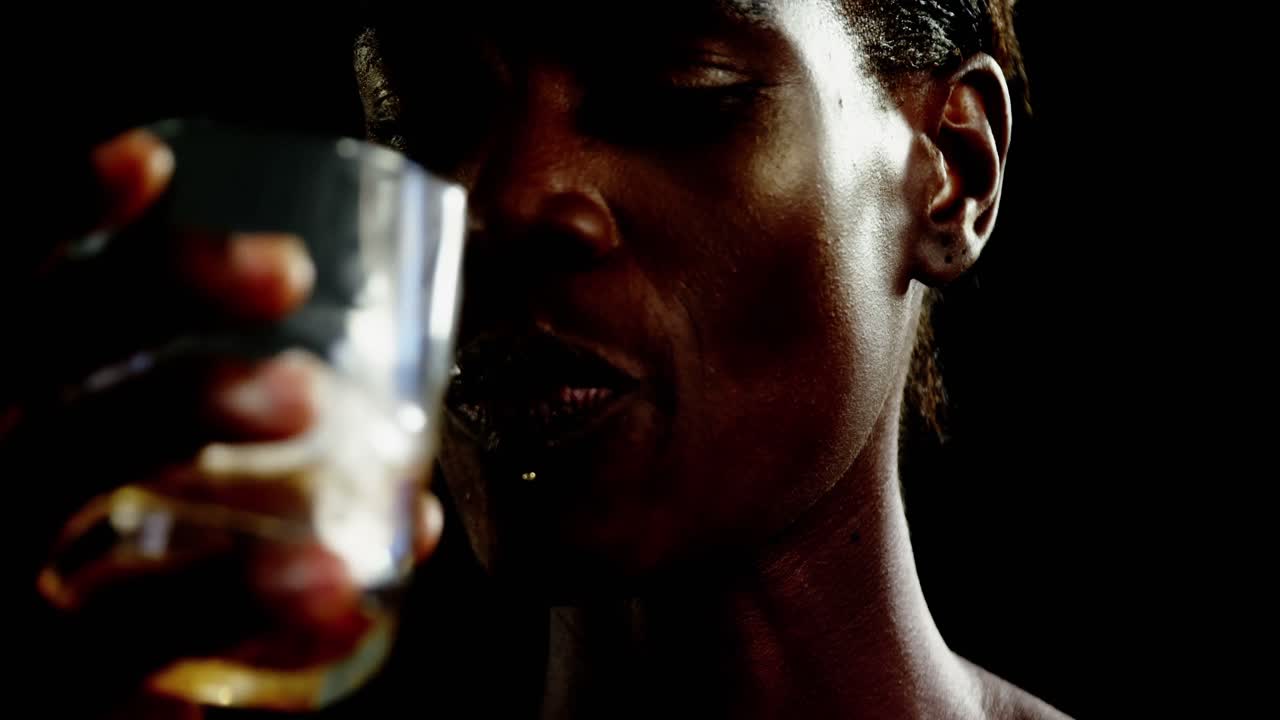 Androgynous man drinking whiskey against black background