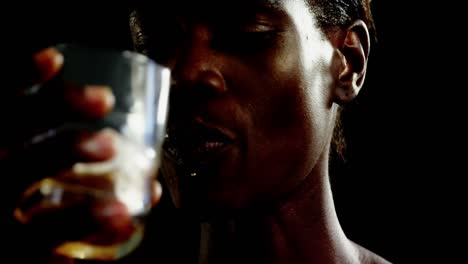 Androgynous-man-drinking-whiskey-against-black-background