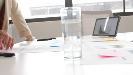 Hands-of-biracial-casual-businesswoman-in-hijab-using-notes-and-tablet-in-meeting-room,-slow-motion