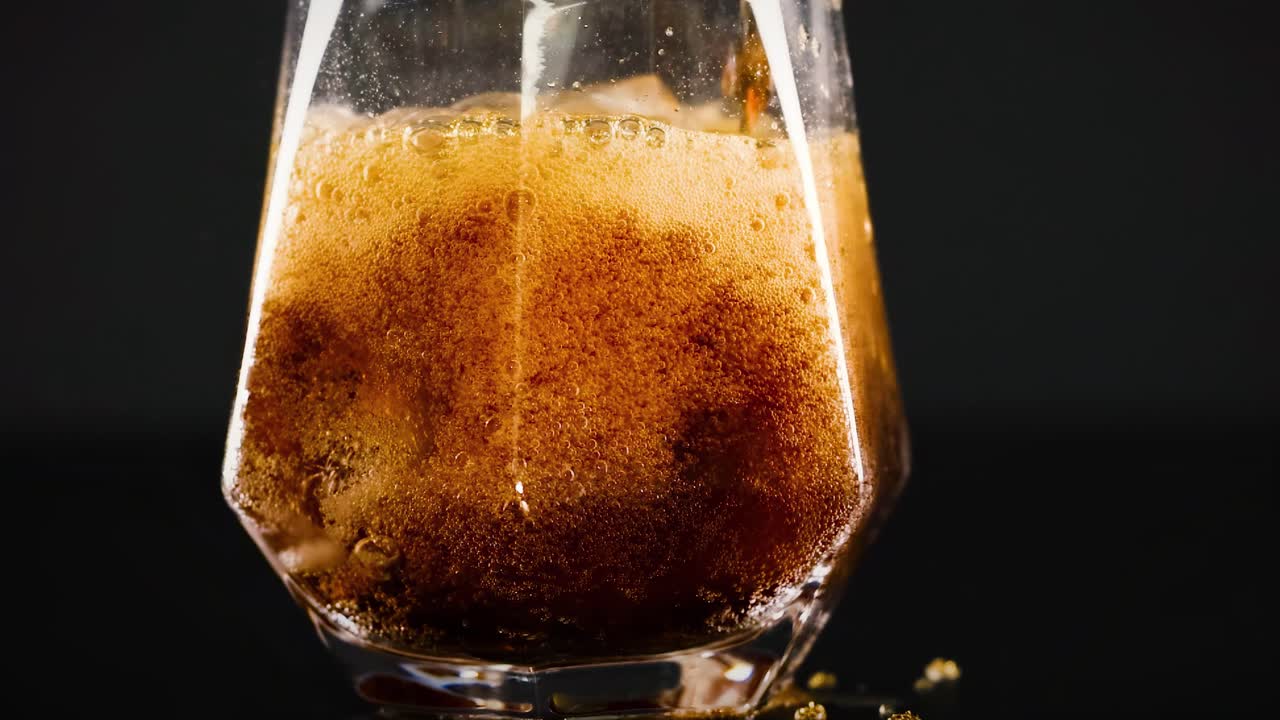 A detailed view of soda being poured into a glass filled with ice, showcasing bubbles and fizz.