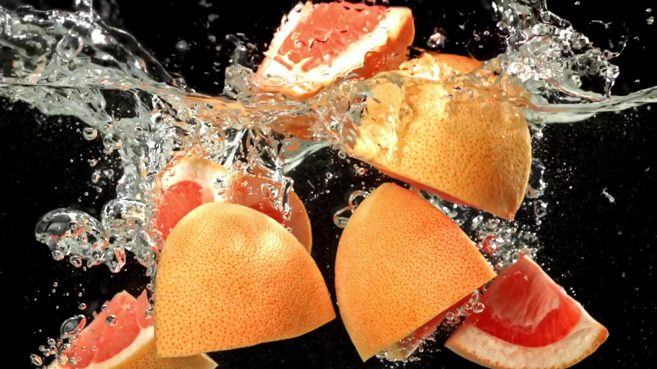 Friske grapefruktskiver plasker ned i vann i sakte film