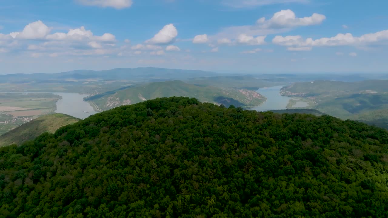 volando sobre una montaña forestal donde hay un río detrás de ella con un barco, en un día soleado y nublado con cielo azul