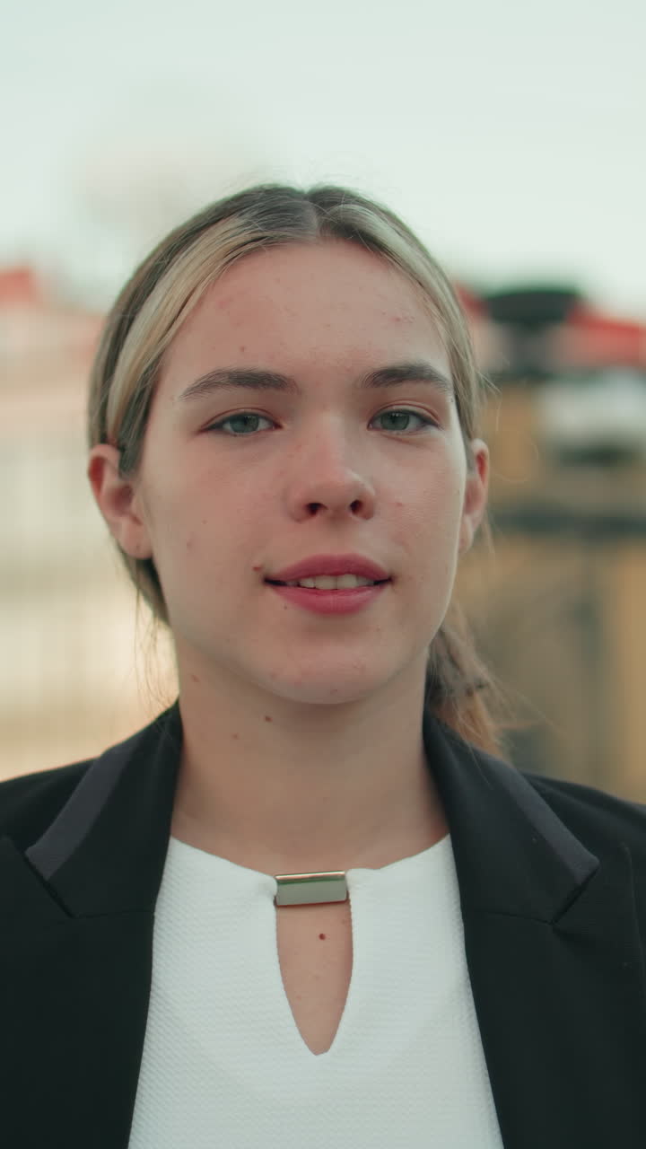 Elegant kvinde i professionelt tøj står selvsikkert udendørs med hænderne i siden og udstråler selvtillid i et moderne bymiljø med en arkitektonisk baggrund og slørede mennesker, der går forbi bag hende