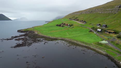 drone voando para trás revela uma paisagem verde faroese e nublada com casas de telhado de relva em kirkjubour