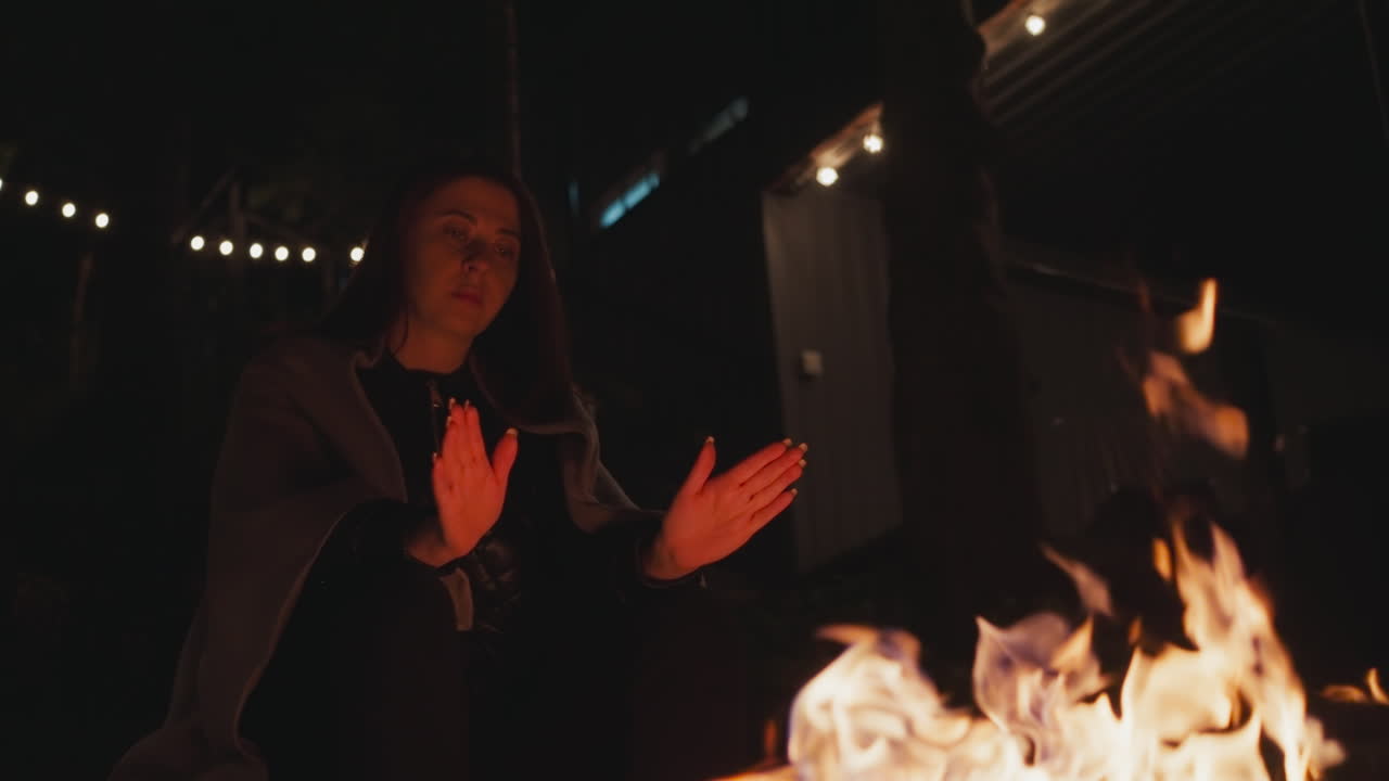 mujer extiende las manos palmas hasta el fuego. mujer joven se esfuerza por calentar las manos en la noche fría participando en la contemplación reflexiva. mujer en manta