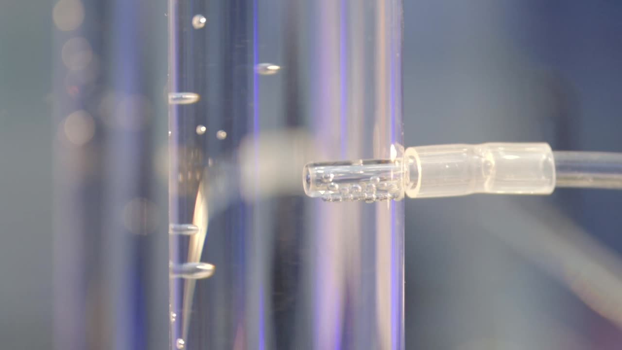 Bubbles of hydrogen gas flow from an electrolyzer into a glass cylinder filled with water, slow motion, HD Crop