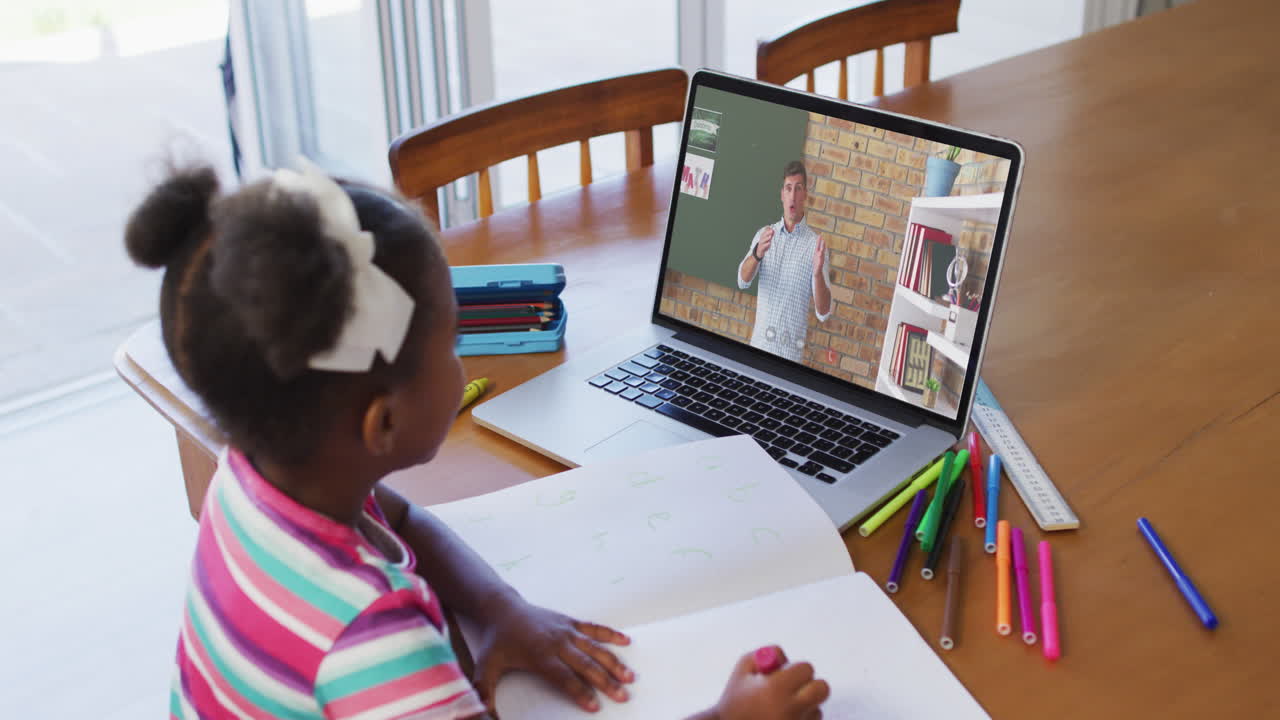 African american girl doing homework while having a video call with male teacher on laptop at home