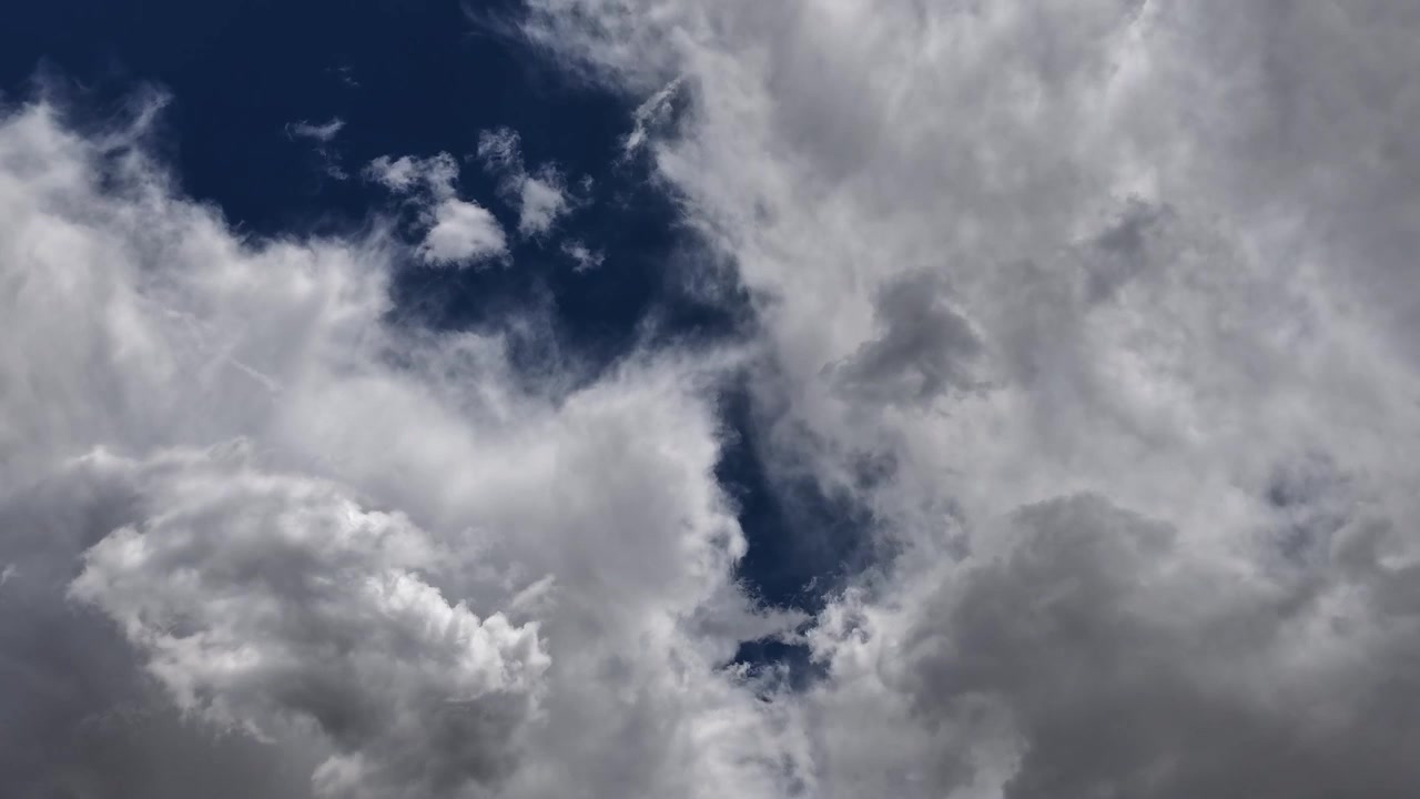 4K timelapse of a shifting climate and dynamic weather system. Intense southwestern light casts high contrast chrome and grey shadows across heavy cloud formations against a deep blue sky.