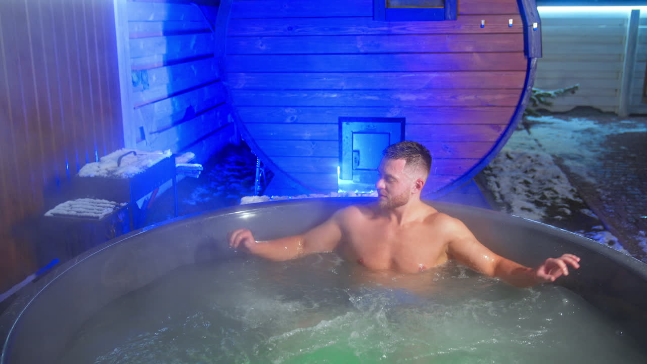 Bearded muscular Caucasian man sits in the jacuzzi. Spa relaxation outdoors in winter. Top view.